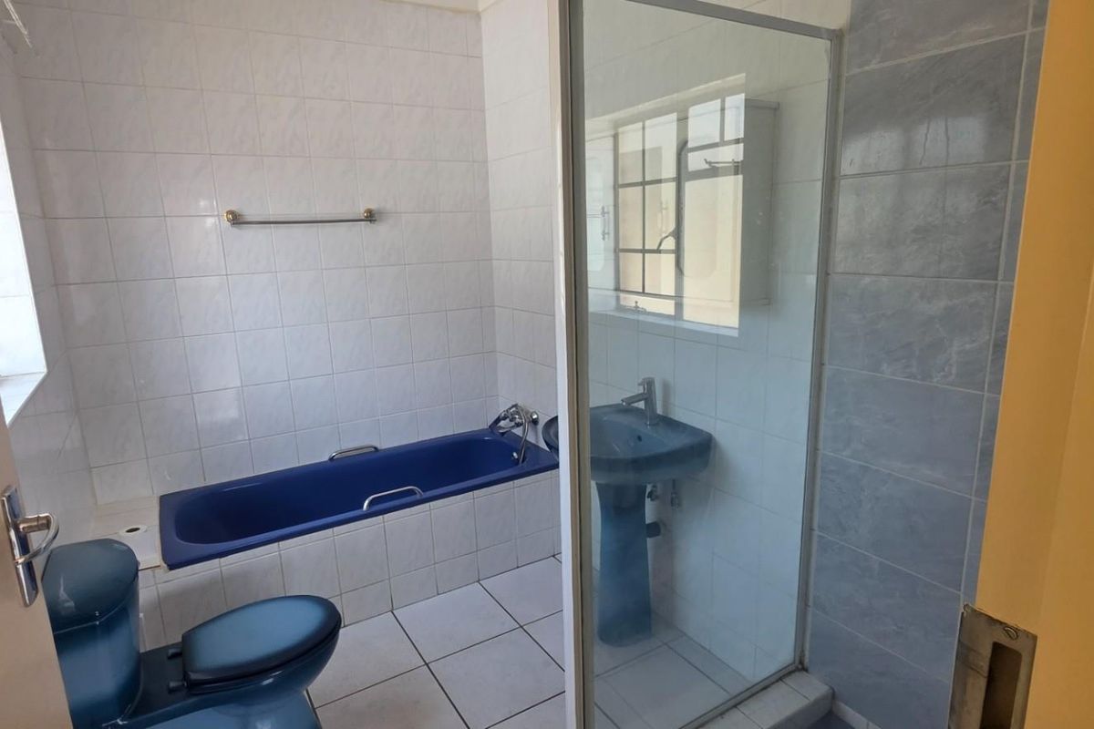 A functional bathroom featuring a built-in bathtub, pedestal basin, toilet, and a separate glass-enclosed shower with tiled finishes throughout.