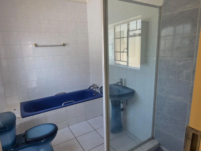 A functional bathroom featuring a built-in bathtub, pedestal basin, toilet, and a separate glass-enclosed shower with tiled finishes throughout.