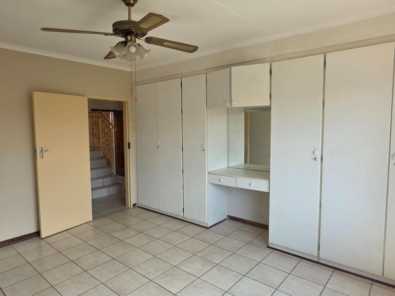 Spacious bedroom featuring built-in cupboards with an integrated vanity, tiled flooring, and a ceiling fan, with an adjacent bathroom and hallway access.
