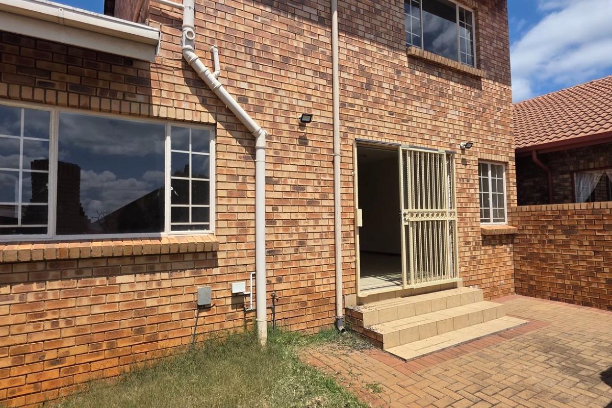 Rear view of a double-story face brick house featuring a paved courtyard, tiled patio steps, and secure entrance gate.