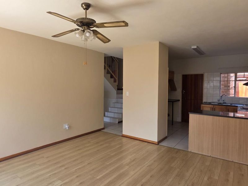 An open-plan living area featuring laminate flooring, a ceiling fan, and an adjacent kitchen with built-in cabinetry and a breakfast counter.