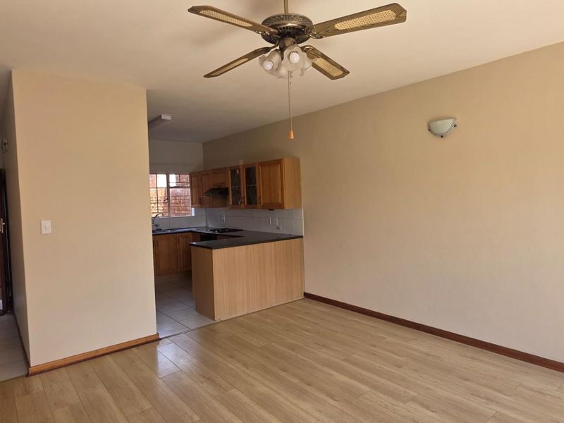Open plan living area featuring laminate flooring, a ceiling fan, and a functional kitchen with built-in cabinetry and countertops.