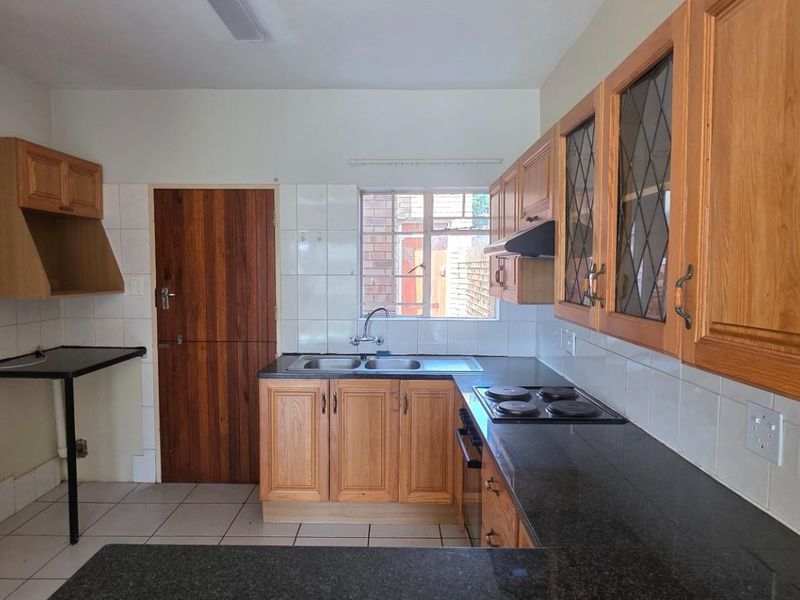 A functional kitchen featuring wooden cabinetry, granite countertops, a built-in hob, and tiled finishes, offering a clean and practical workspace.