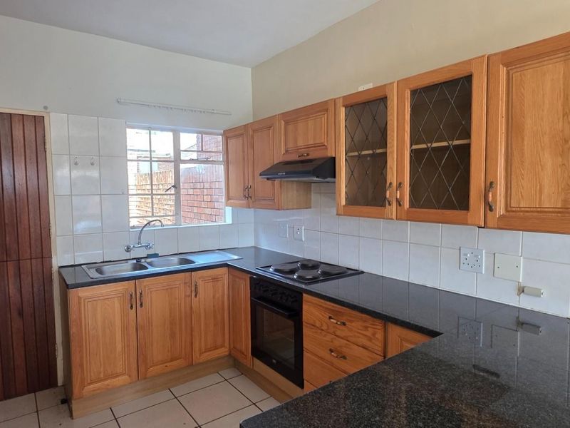 A functional kitchen featuring wooden cabinetry, granite countertops, a built-in oven with hob, and tiled finishes throughout.