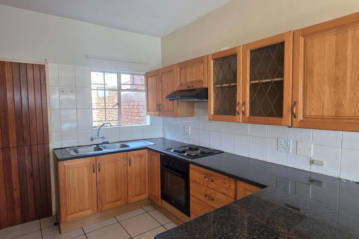 A functional kitchen featuring wooden cabinetry, granite countertops, a built-in oven with hob, and tiled finishes throughout.