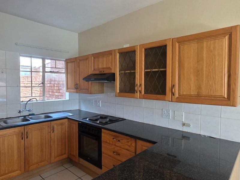 A functional kitchen featuring wooden cabinetry, granite countertops, a built-in oven with hob, and a double basin sink with tiled splashbacks.