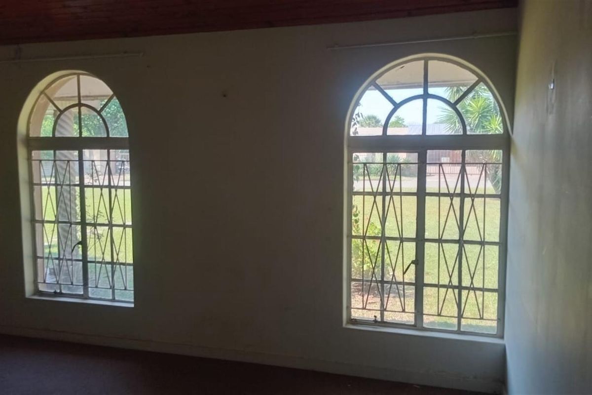 An empty room featuring two arched windows with security bars and a wooden ceiling finish.