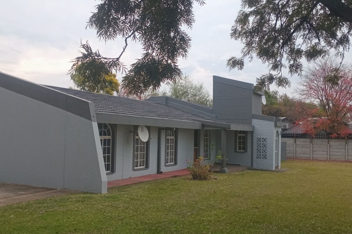 A view of the exterior rear of the property, featuring a tiled roof, painted brick facade, and a spacious lawn area.