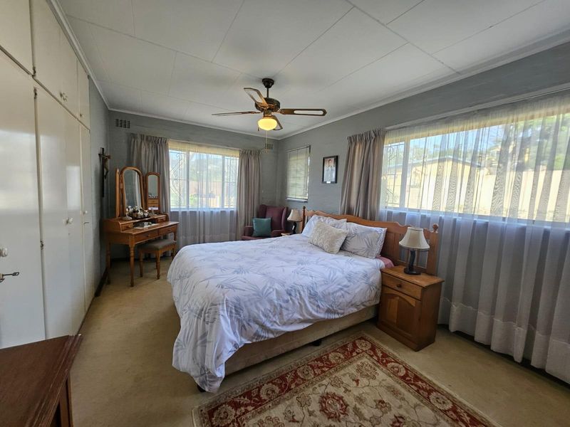 A spacious bedroom featuring built-in cupboards, a ceiling fan, and large windows that provide ample natural light.