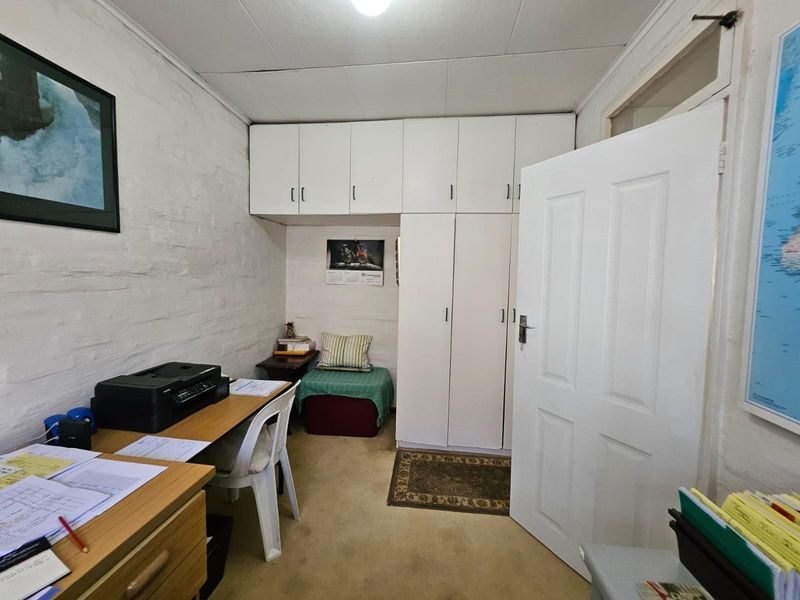 A functional bedroom featuring built-in cupboards with overhead storage, painted brick walls, and carpeted flooring.