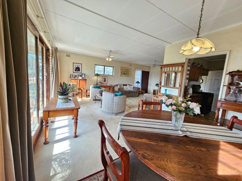 Spacious open-plan living and dining area featuring carpeted floors, ceiling fans, and large sliding glass doors providing ample natural light.