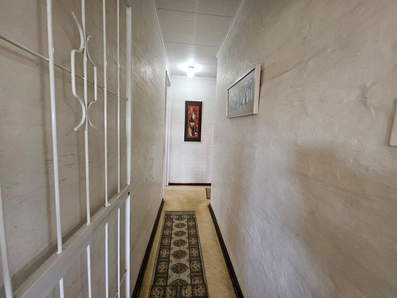 A narrow residential hallway featuring textured walls, a security gate, and neutral flooring, providing access to other areas of the home.