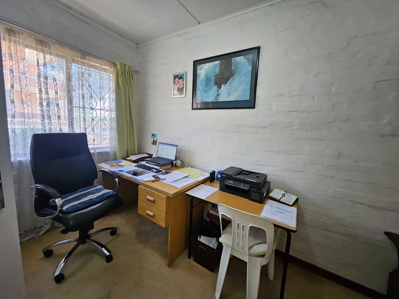 A functional home office space featuring a painted brick wall and a window fitted with security bars.
