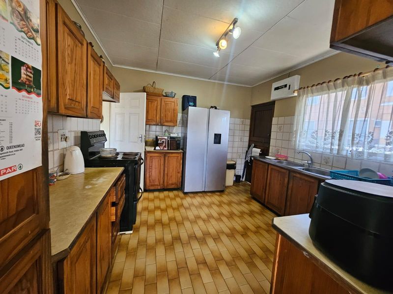 A functional kitchen featuring wooden cabinetry, tiled backsplash, double sink, and tiled flooring, offering potential for modernization and aesthetic updates.