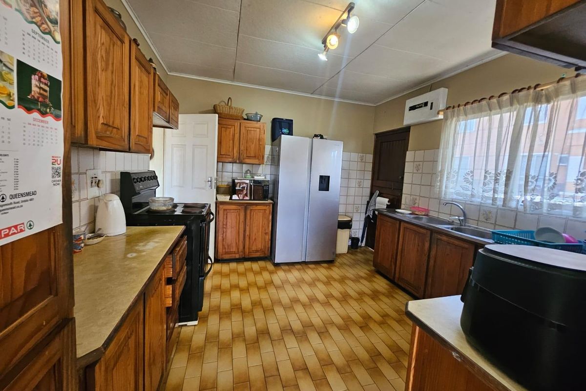 A functional kitchen featuring wooden cabinetry, tiled backsplash, double sink, and tiled flooring, offering potential for modernization and aesthetic updates.