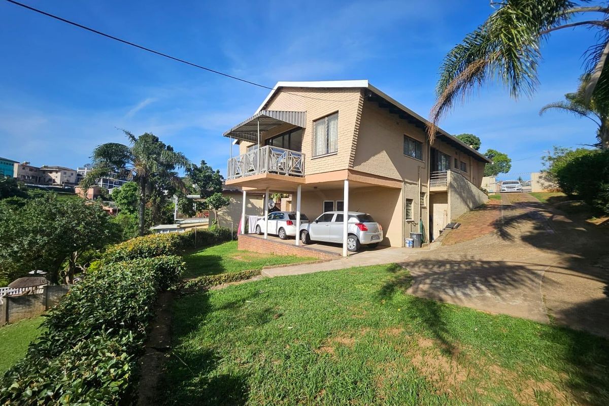 Rear view of a multi-level brick house featuring a balcony, covered parking area, and a sloped garden with a concrete driveway.