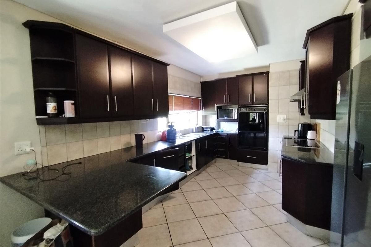 Spacious kitchen featuring dark wood cabinetry, granite countertops, tiled flooring, and integrated oven and hob.