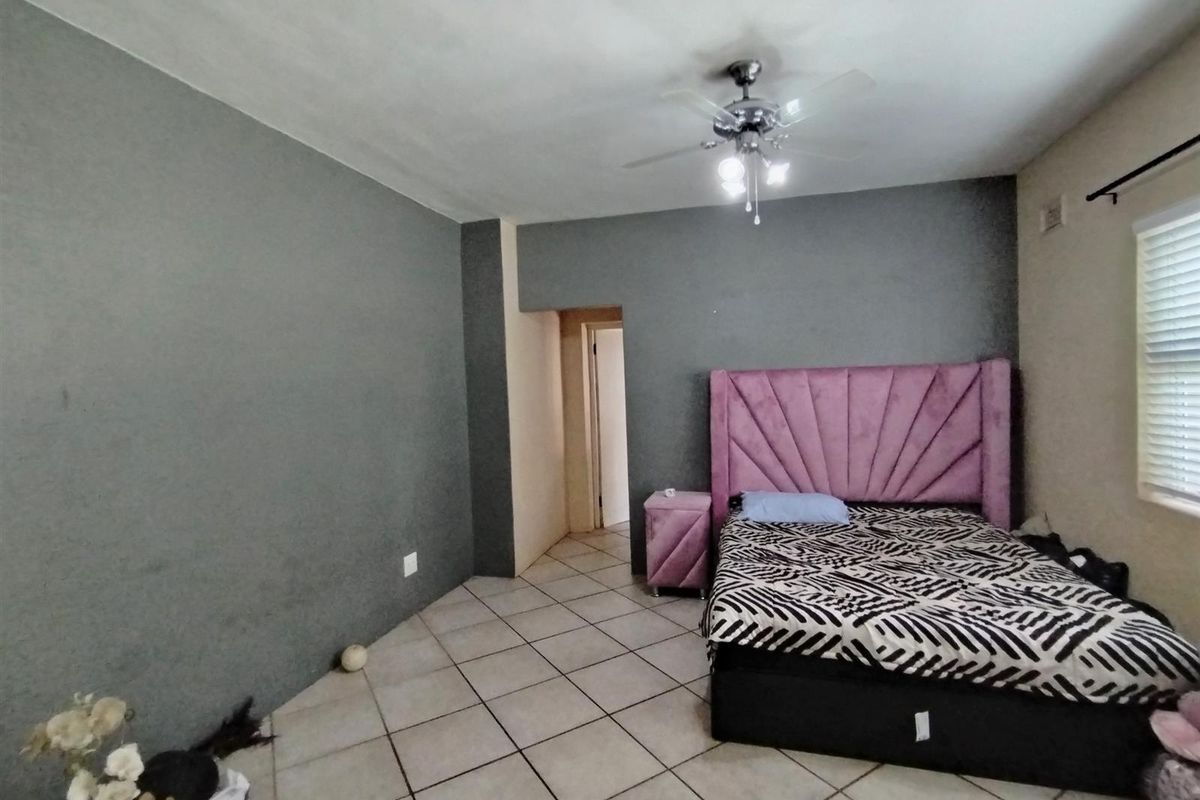 A bedroom featuring tiled flooring, a ceiling fan, and a neutral grey accent wall.