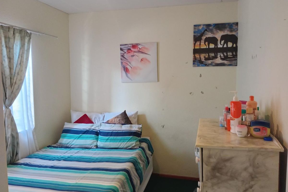 A compact bedroom featuring a window with curtains and dark flooring, requiring minor cosmetic updates to the wall surfaces.