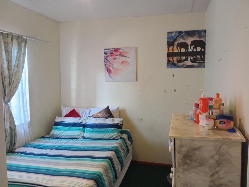A compact bedroom featuring a window with curtains and dark flooring, requiring minor cosmetic updates to the wall surfaces.