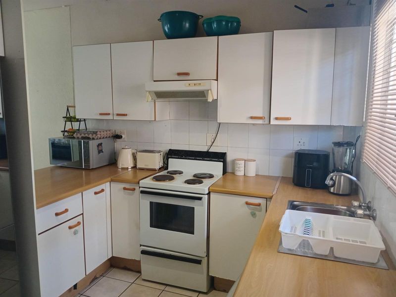 A functional kitchen featuring white cabinetry, wood-look laminate countertops, a freestanding electric stove with extractor fan, and a stainless steel sink.