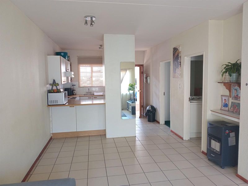 Open plan living area featuring tiled flooring, a compact kitchen with built-in cabinetry, and access to adjacent rooms.