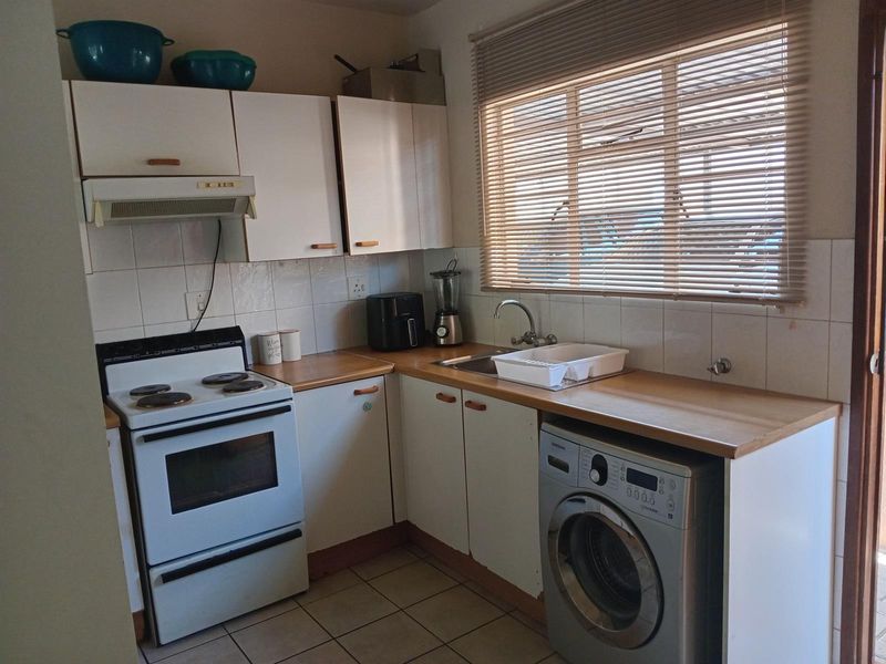 Compact kitchen featuring white cabinetry, wood-look countertops, tiled backsplash, built-in stove with extractor fan, and plumbing connection for a washing machine.