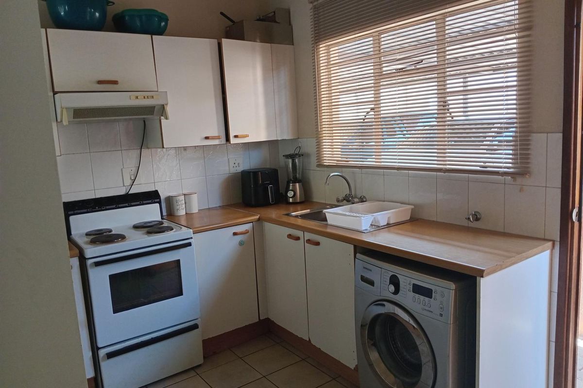 Compact kitchen featuring white cabinetry, wood-look countertops, tiled backsplash, built-in stove with extractor fan, and plumbing connection for a washing machine.