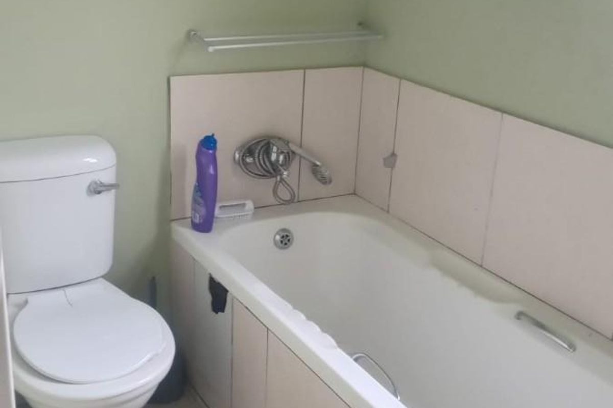 A functional bathroom featuring a standard bathtub with integrated shower mixer, tiled splashback, and a white ceramic toilet.
