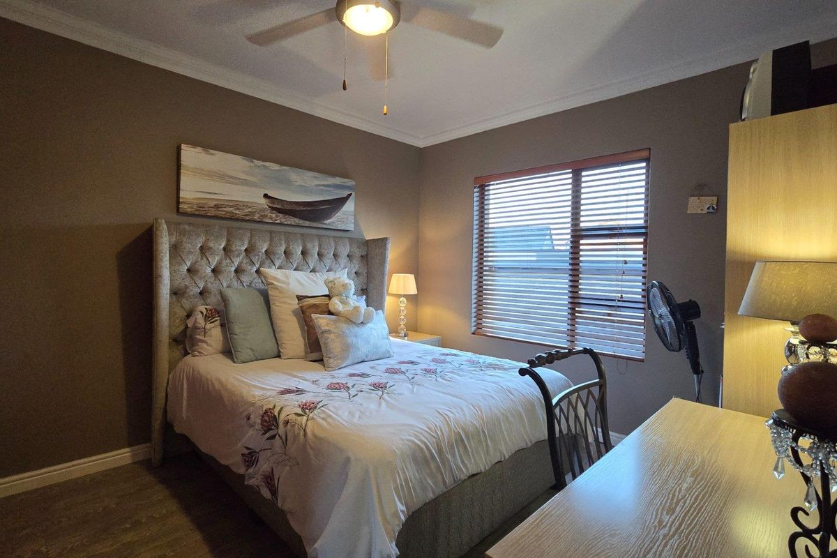 A cozy bedroom featuring a ceiling fan, wooden window blinds, and neutral wall tones, providing a comfortable and functional living space.