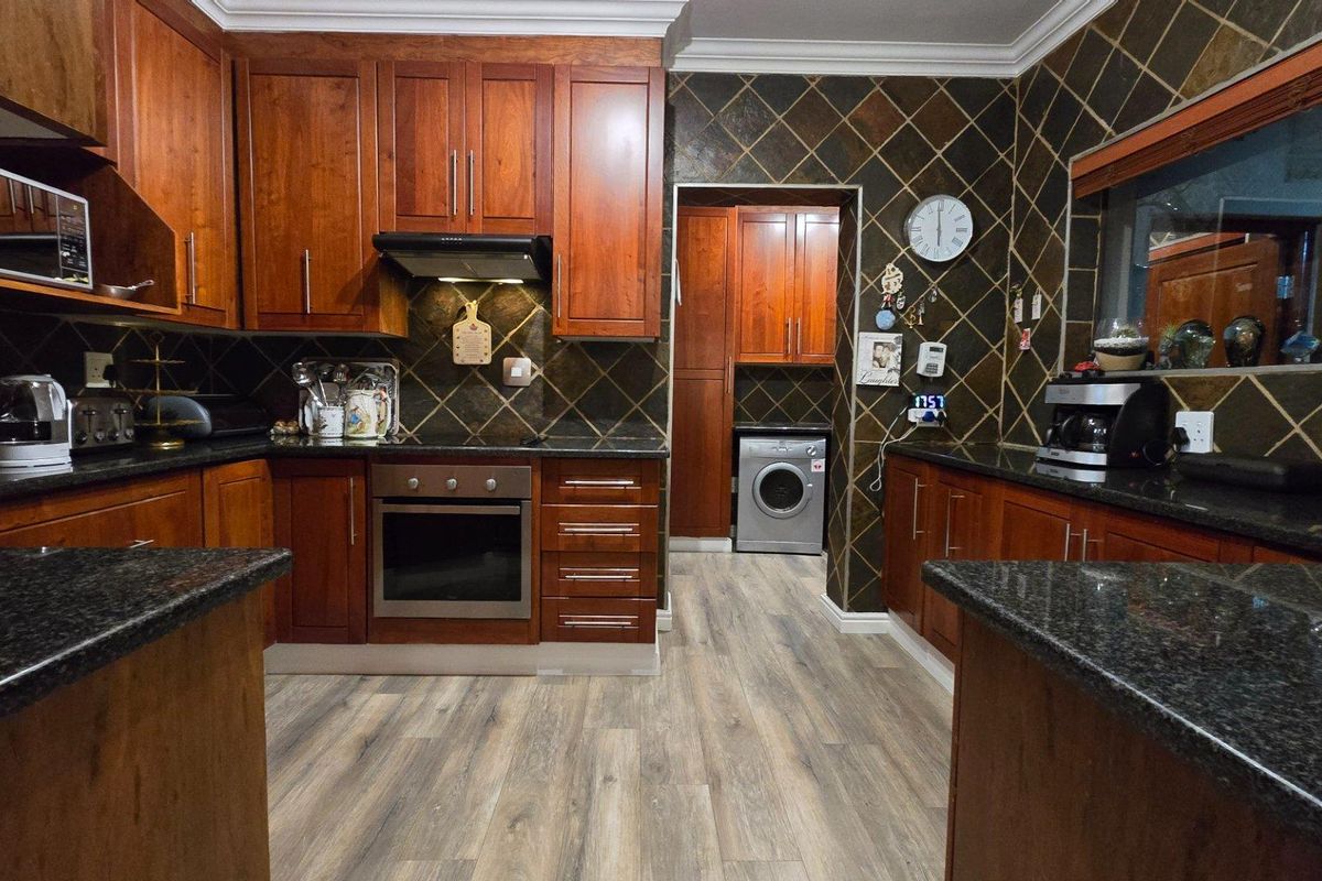 A functional kitchen featuring dark granite countertops, wood-finish cabinetry, a built-in oven, and a tiled backsplash, with an adjacent laundry area.