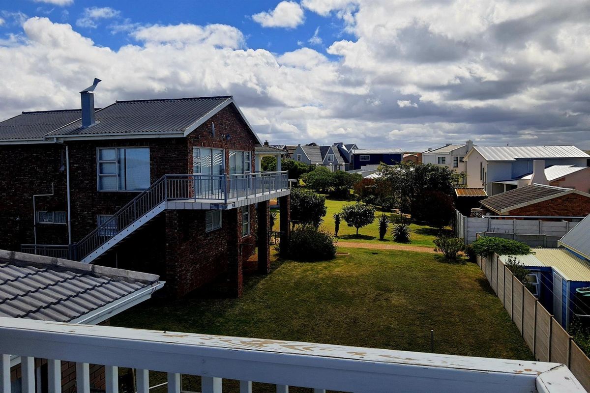 Elevated view of a brick residential property featuring a balcony, metal roof, and surrounding garden area within a suburban neighborhood.