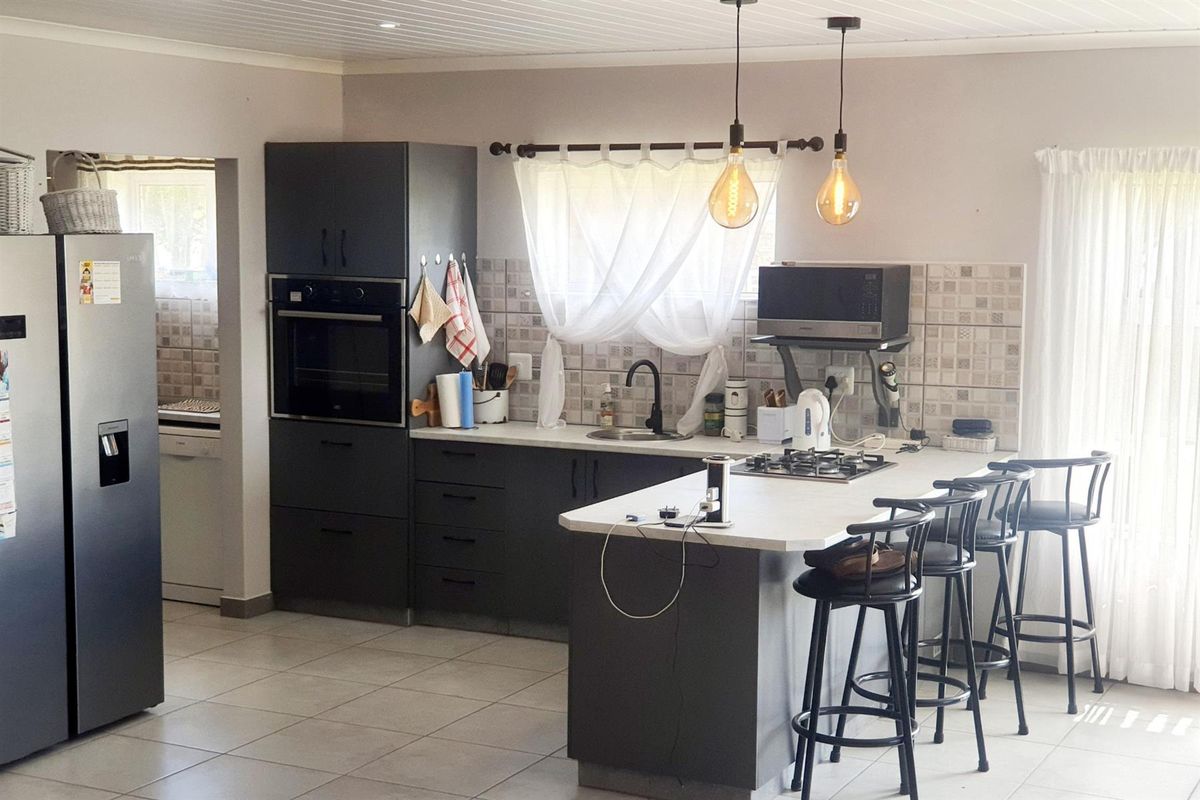 Modern kitchen featuring dark cabinetry, a central island with a gas hob, built-in oven, and tiled flooring, with an adjacent scullery area.