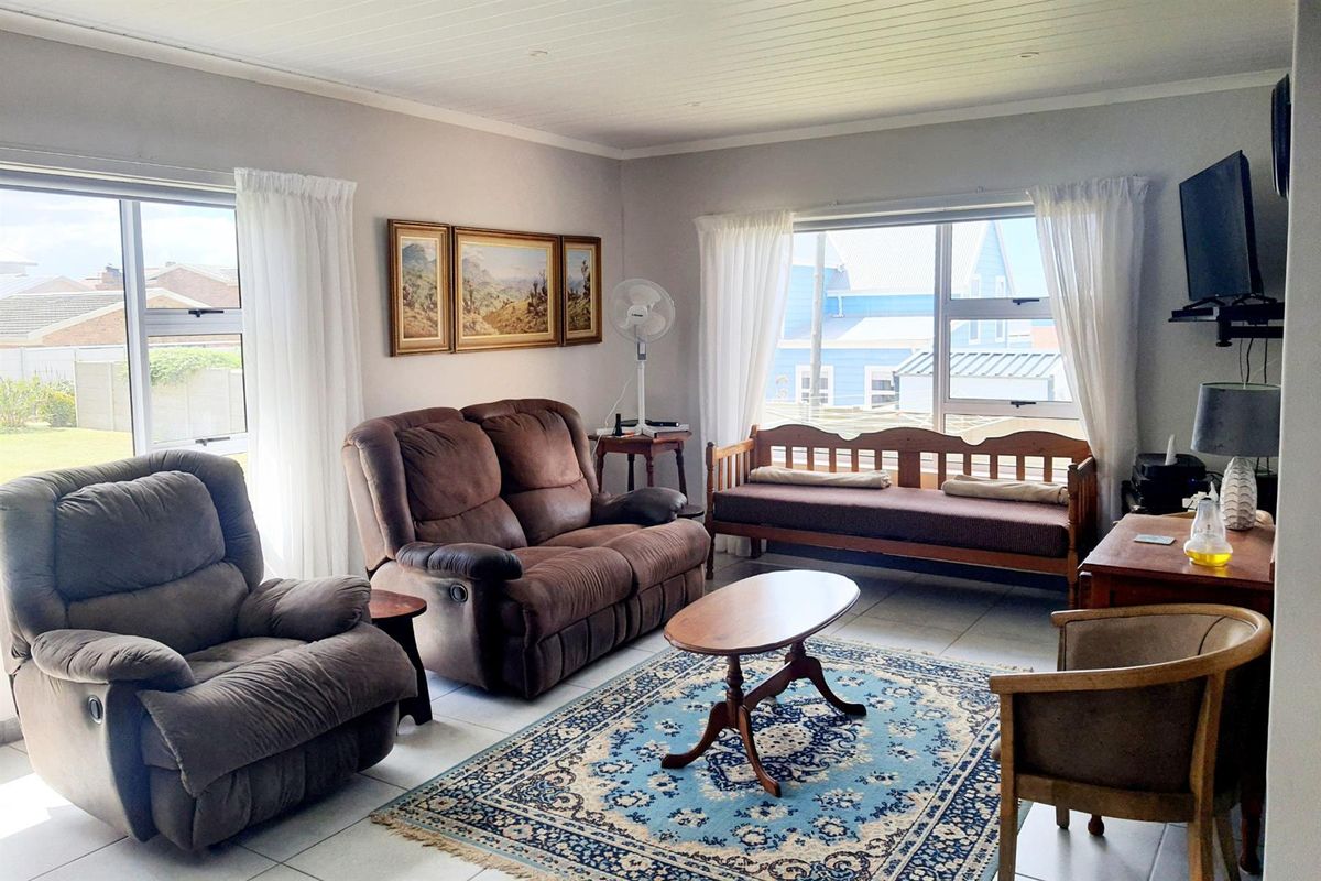A bright and spacious living room featuring large windows, tiled flooring, and a classic tongue-and-groove ceiling finish.