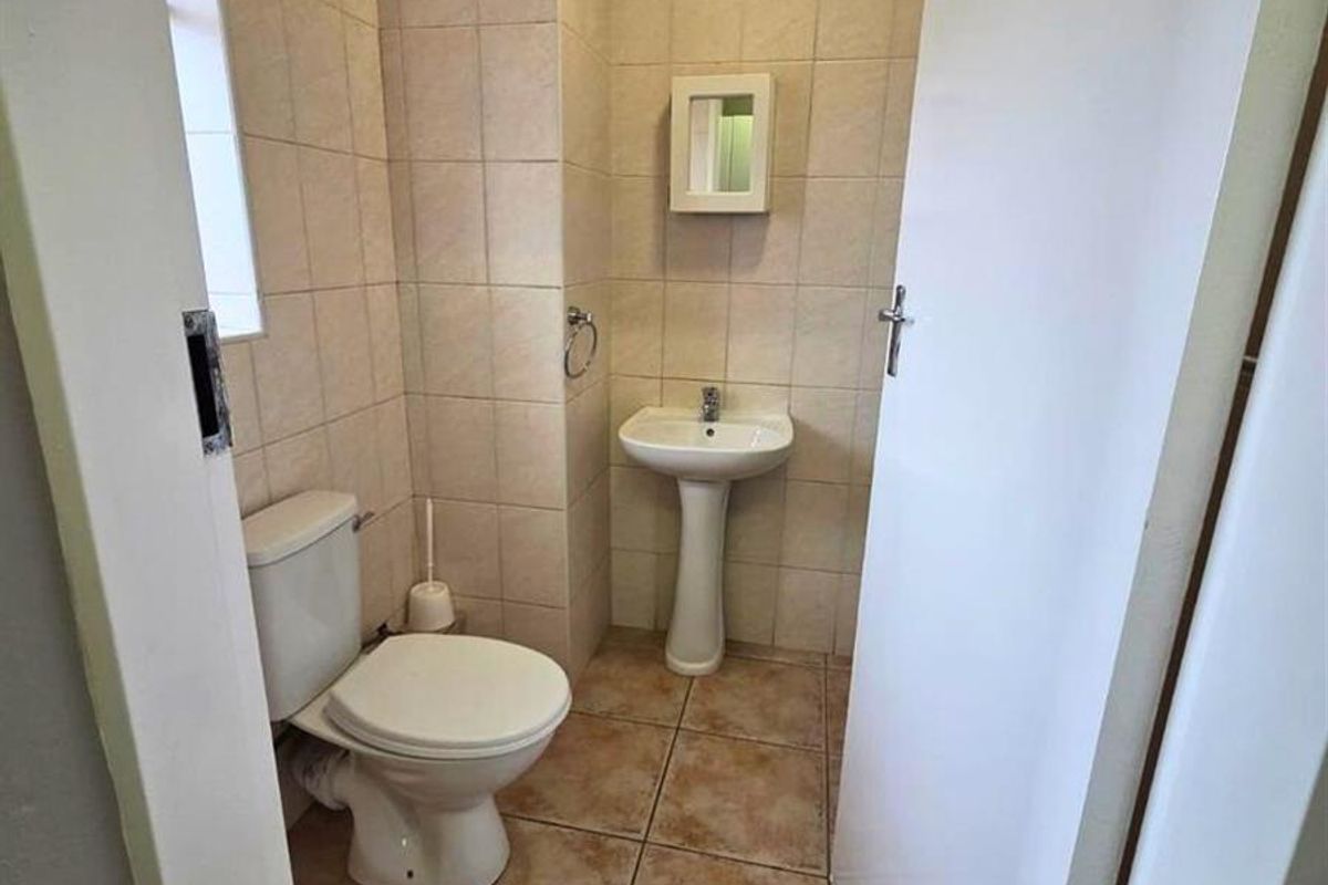 A compact guest bathroom featuring a pedestal basin, standard toilet, and neutral floor-to-ceiling wall tiles.