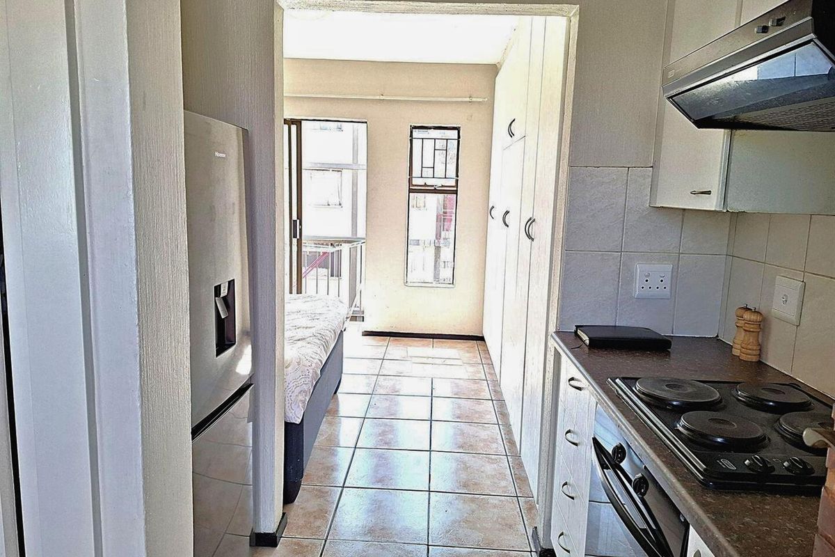 A functional kitchen area featuring built-in cabinetry, a stove with extractor fan, and tiled flooring, leading into an adjacent living space.
