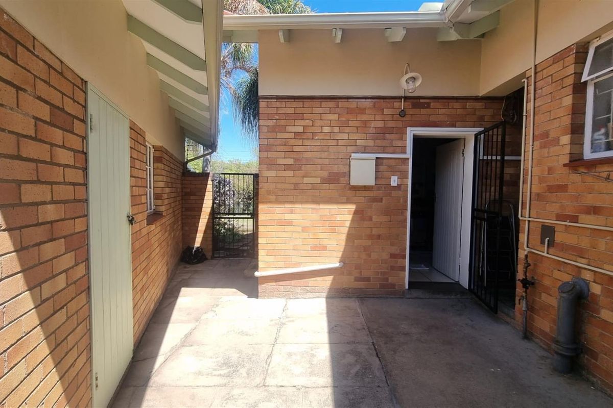 A functional rear courtyard area featuring exposed brick walls, paved flooring, and secure gated access to the garden.