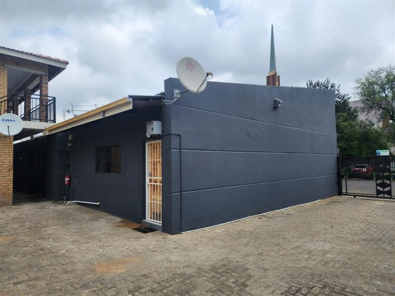 Rear exterior view of the apartment building featuring a dark painted facade, security gate, and paved driveway area.