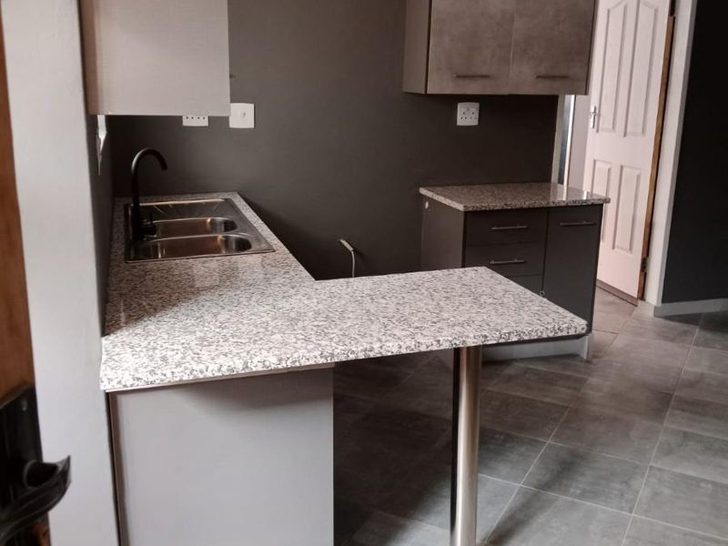 A modern, clean kitchen featuring granite countertops, a breakfast bar, stainless steel sink, and contemporary cabinetry with neutral grey tones.