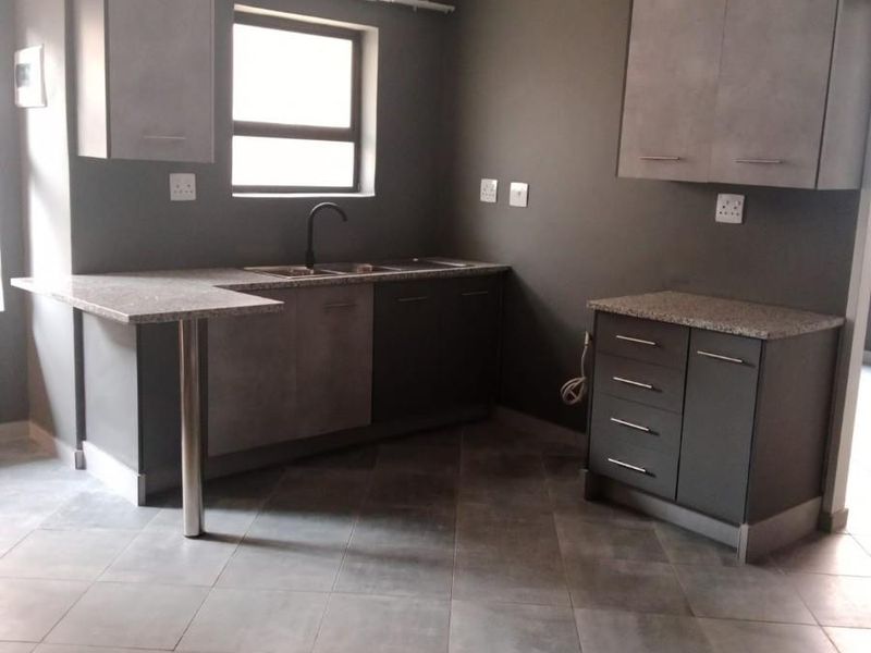 A modern, empty kitchen featuring grey cabinetry, granite countertops, a stainless steel sink, and tiled flooring, offering a clean and functional workspace.