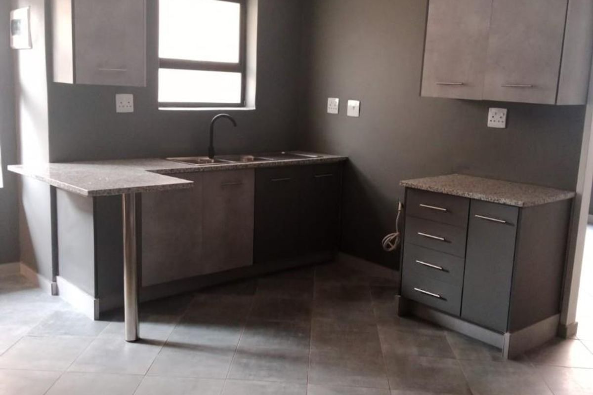 A modern, empty kitchen featuring grey cabinetry, granite countertops, a stainless steel sink, and tiled flooring, offering a clean and functional workspace.