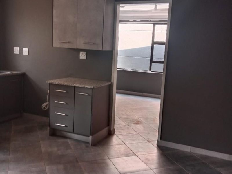 A compact kitchen area featuring modern grey cabinetry, granite countertops, and tiled flooring, leading into an adjacent room.
