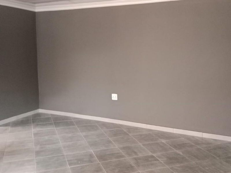An empty living area featuring neutral grey walls, tiled flooring, and decorative ceiling cornicing, providing a clean and versatile space.