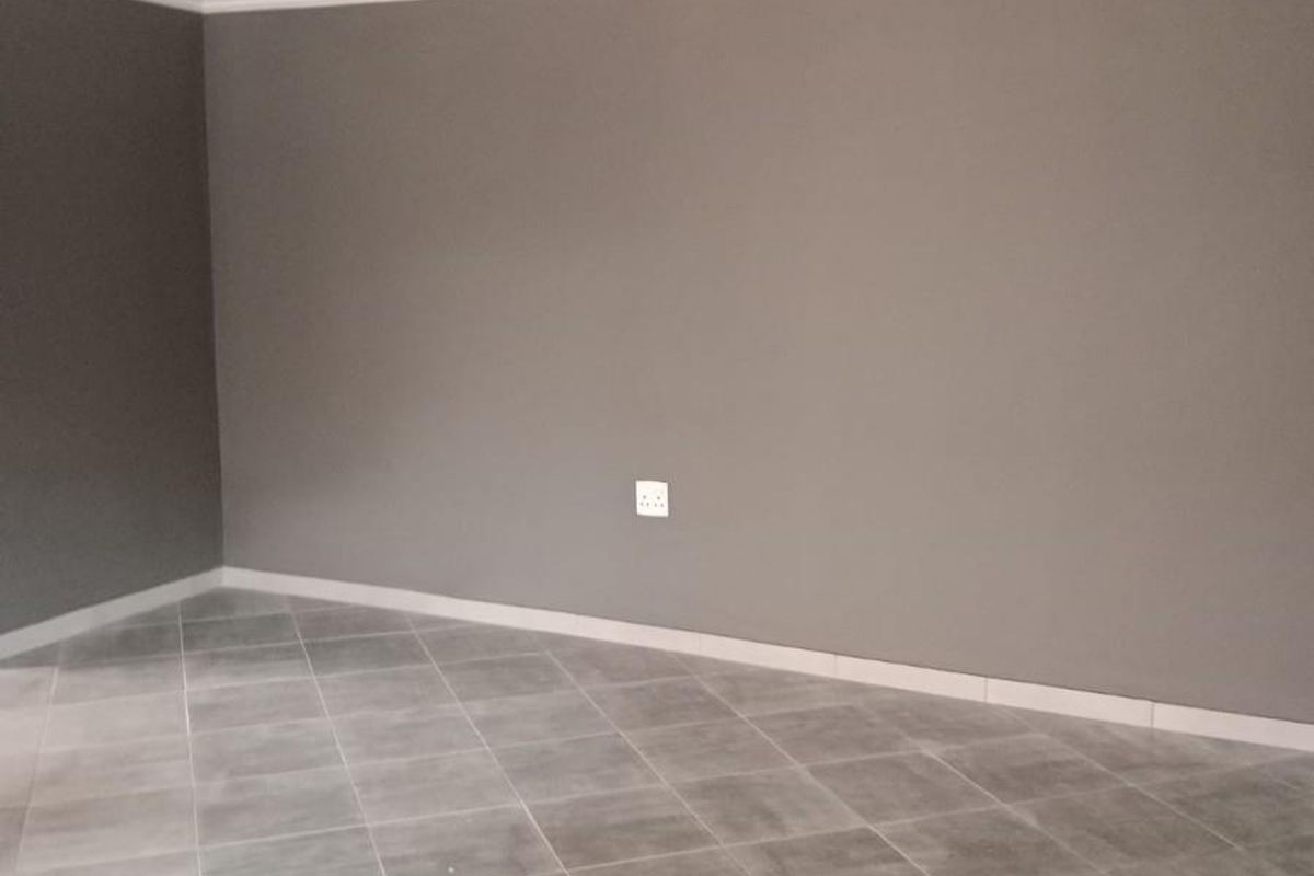 An empty living area featuring neutral grey walls, tiled flooring, and decorative ceiling cornicing, providing a clean and versatile space.