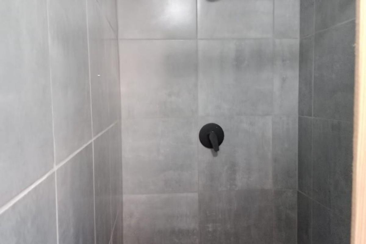A modern shower enclosure featuring grey wall and floor tiles, a black shower mixer, and a standard shower head.