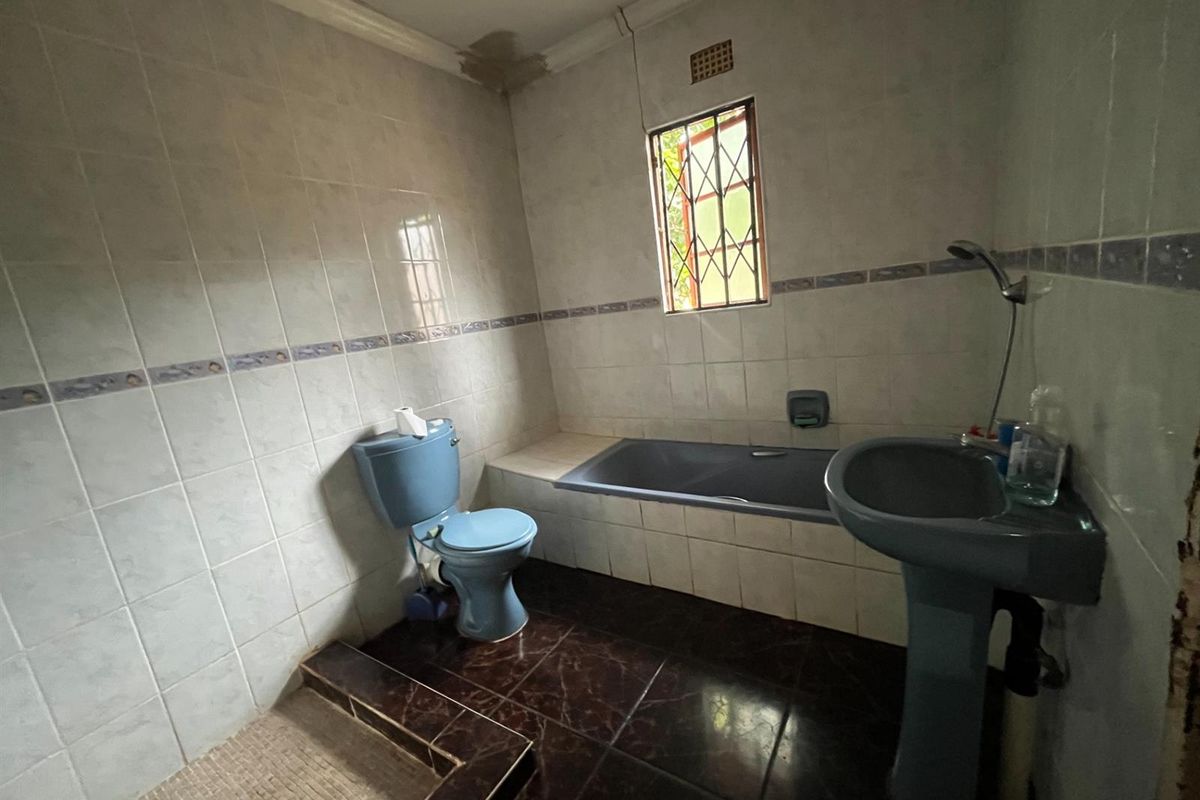 A dated bathroom featuring a blue pedestal basin, matching toilet, and built-in bathtub with tiled surround and dark floor tiles.