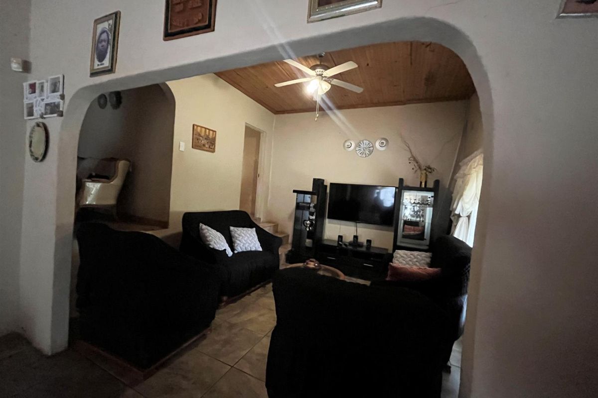 A cozy living room featuring a distinctive arched entryway, tiled flooring, and a timber-paneled ceiling with a central fan.