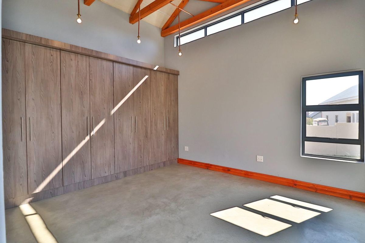 A bright, modern bedroom featuring polished concrete floors, exposed timber roof trusses, and extensive built-in cabinetry with a clean, contemporary aesthetic.