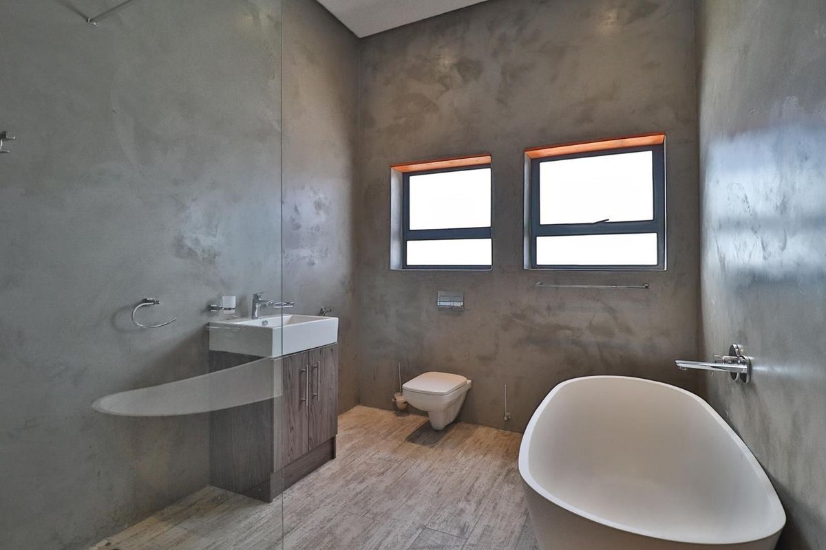 Modern bathroom featuring a freestanding bathtub, wall-mounted toilet, vanity with vessel sink, and contemporary cement-style wall finishes.