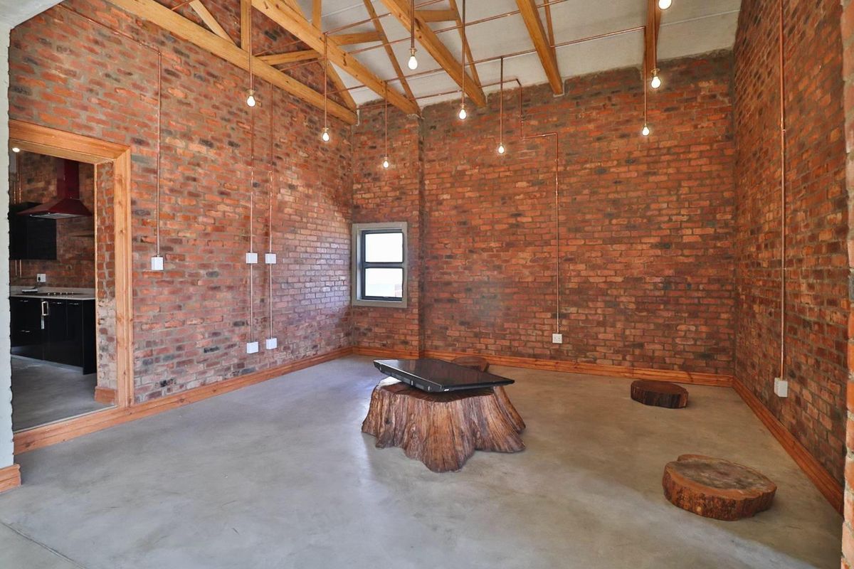 Spacious living area featuring industrial-style exposed brick walls, polished concrete floors, and high timber-trussed ceilings with exposed copper electrical conduits.